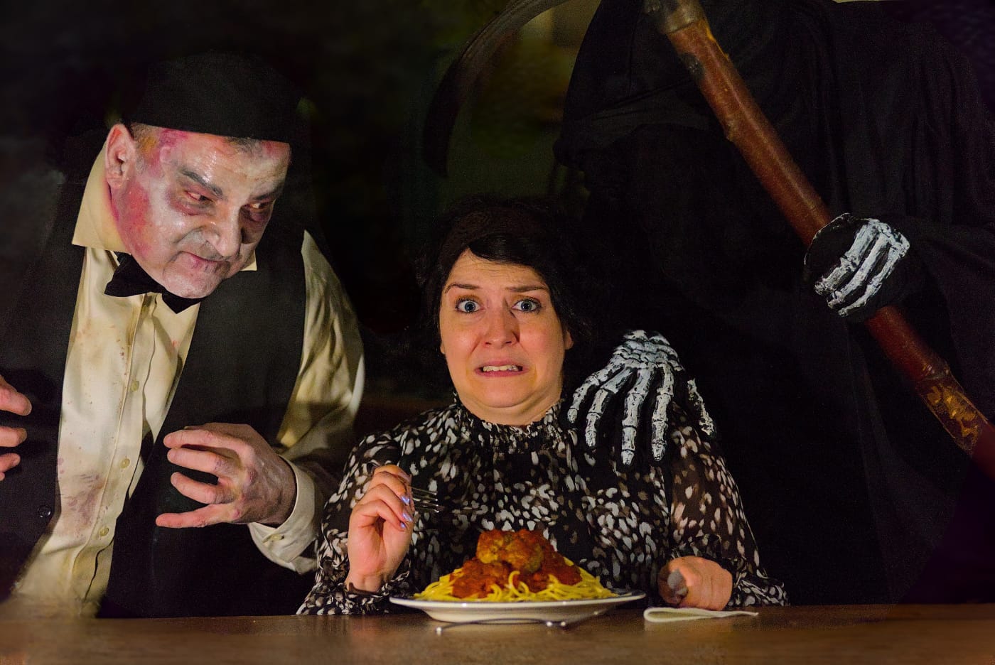 A startled diner flinches as a performer in zombie make-up and a skeletal grim reaper hand close in